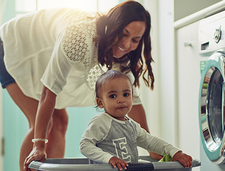 mom of color with toddler sitting in a laundry basket